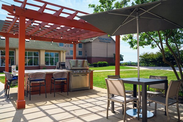 An outdoor patio with a grill, chairs, and a table under a pergola.