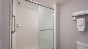 A bathroom with a glass shower enclosure, a white toilet, and a towel rack with two towels.