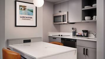 A modern kitchen with a white countertop, stainless steel appliances, and a framed picture on the wall.