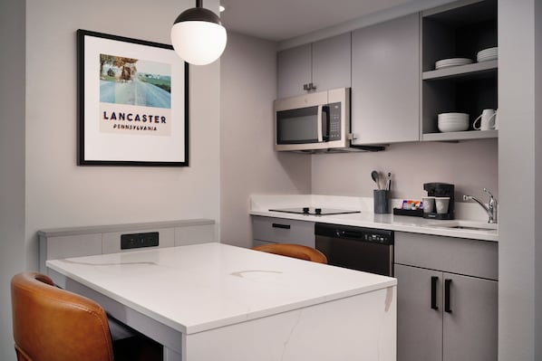 A modern kitchen with a white countertop, stainless steel appliances, and a framed picture on the wall.