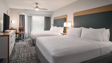 A hotel room with two beds, a desk, a chair, a television, and a ceiling fan.