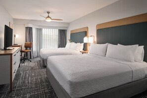 A hotel room with two beds, a desk, a chair, a television, and a ceiling fan.