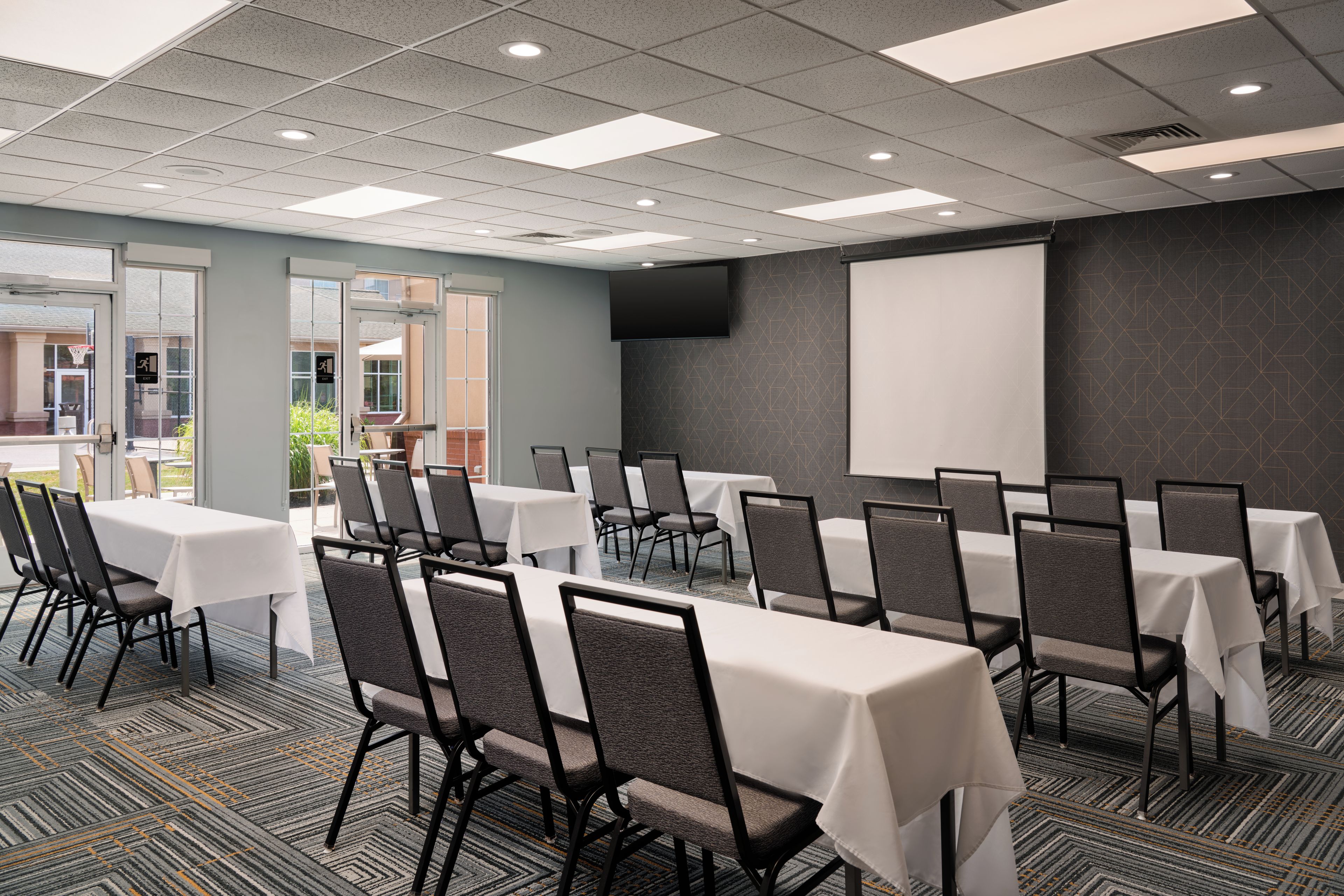 A conference room with multiple tables and chairs, a projector screen, and a large window.