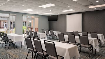 A conference room with multiple tables and chairs, a projector screen, and a large window.