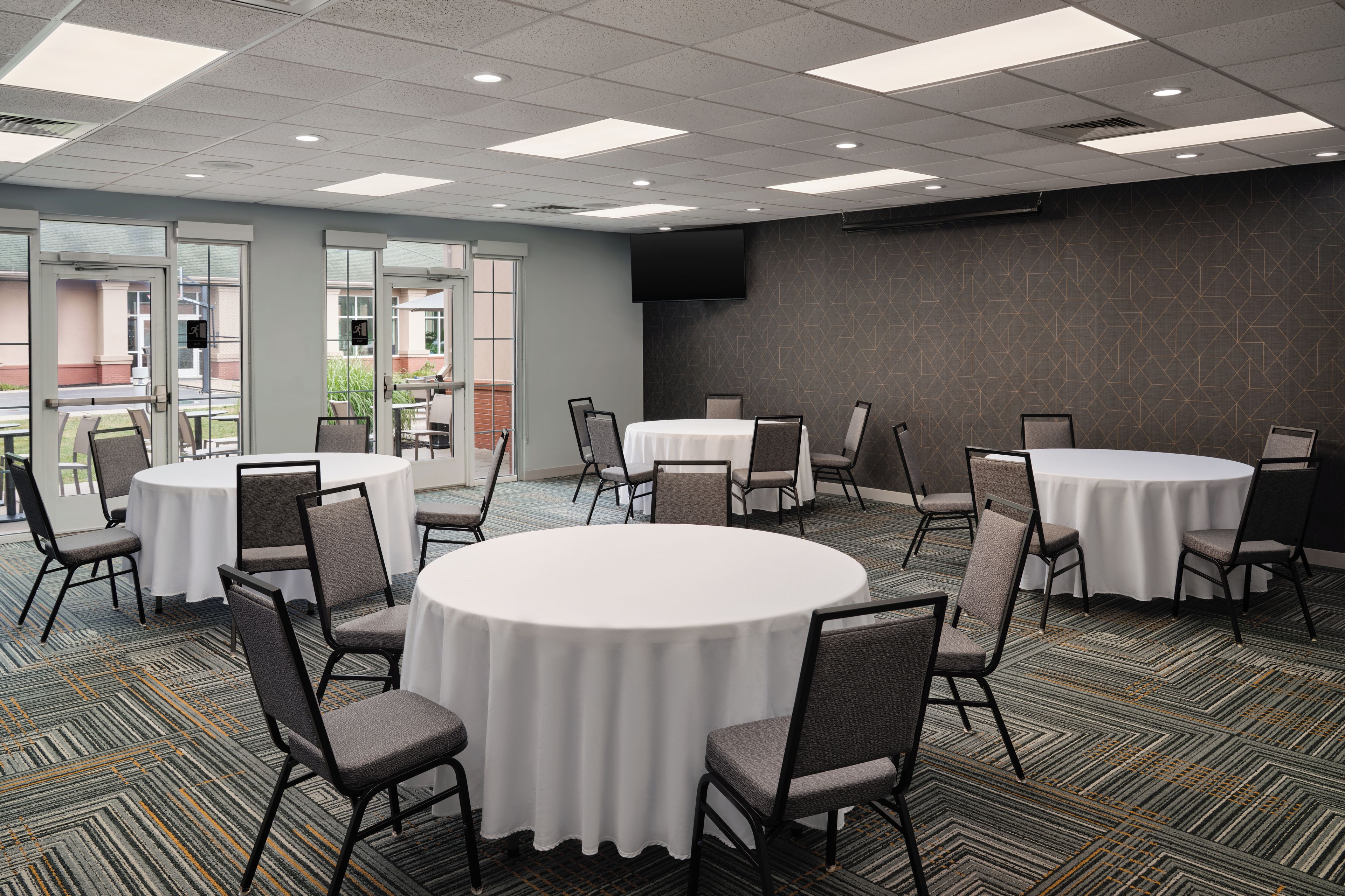 A conference room with round tables, chairs, and a large screen on the wall.