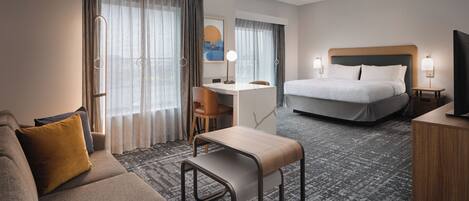 A hotel room with a bed, a desk, a sofa, a chair, a television, and a ceiling fan.