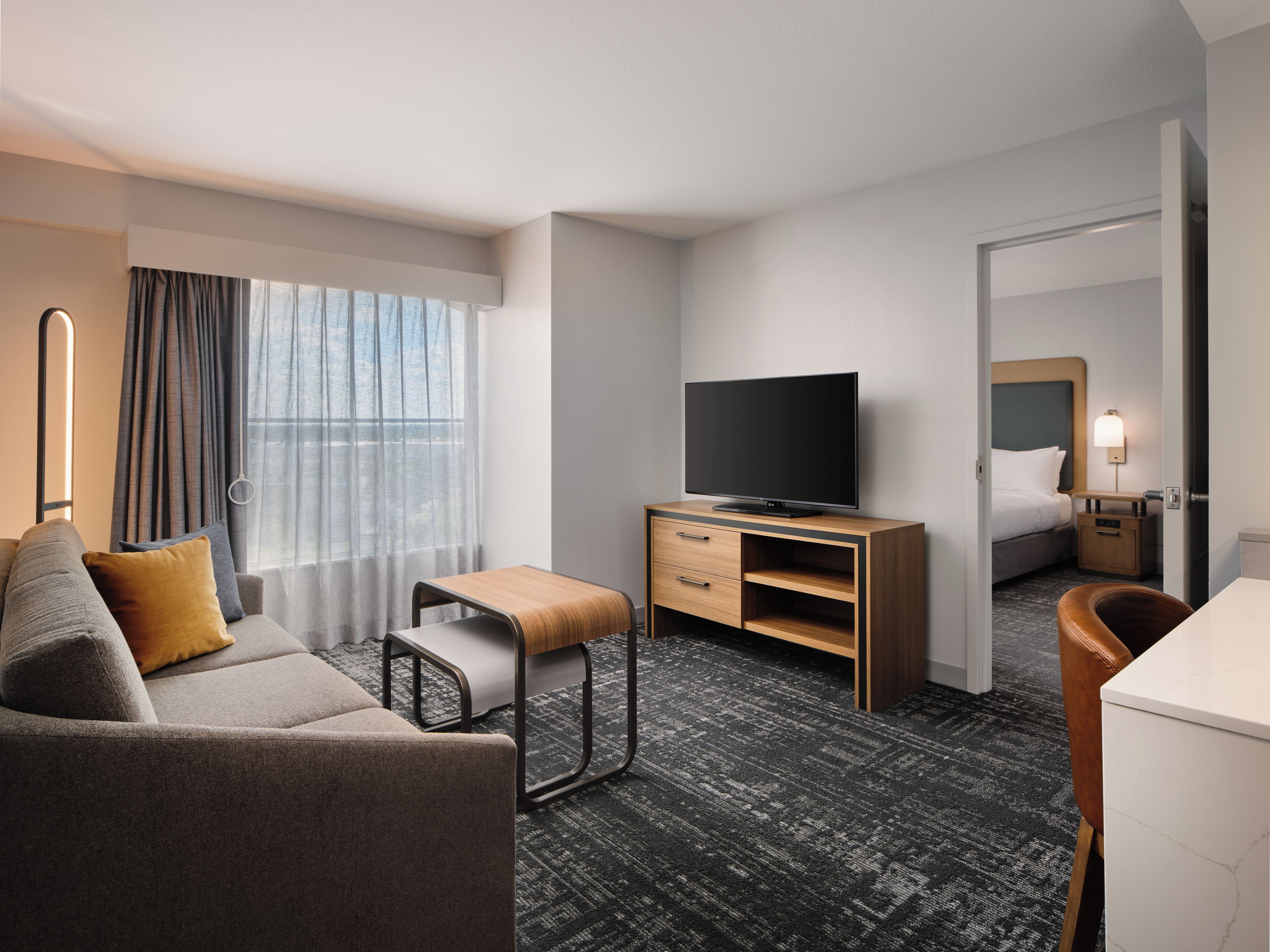 A hotel room with a sofa, a small table, a TV, a bed, a nightstand, and a mirror.