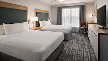 A hotel room with two beds, a desk, a chair, a television, and a ceiling fan.