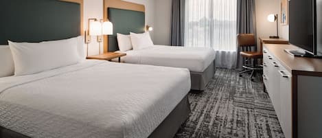 Habitación de hotel con dos camas, un escritorio, una silla, un televisor y un ventilador de techo.