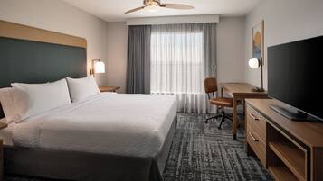A hotel room with a bed, a desk, a chair, a television, and a ceiling fan.