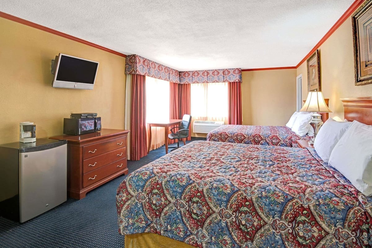 A hotel room with a bed, a desk with a computer, a coffee maker, and a television on the wall.
