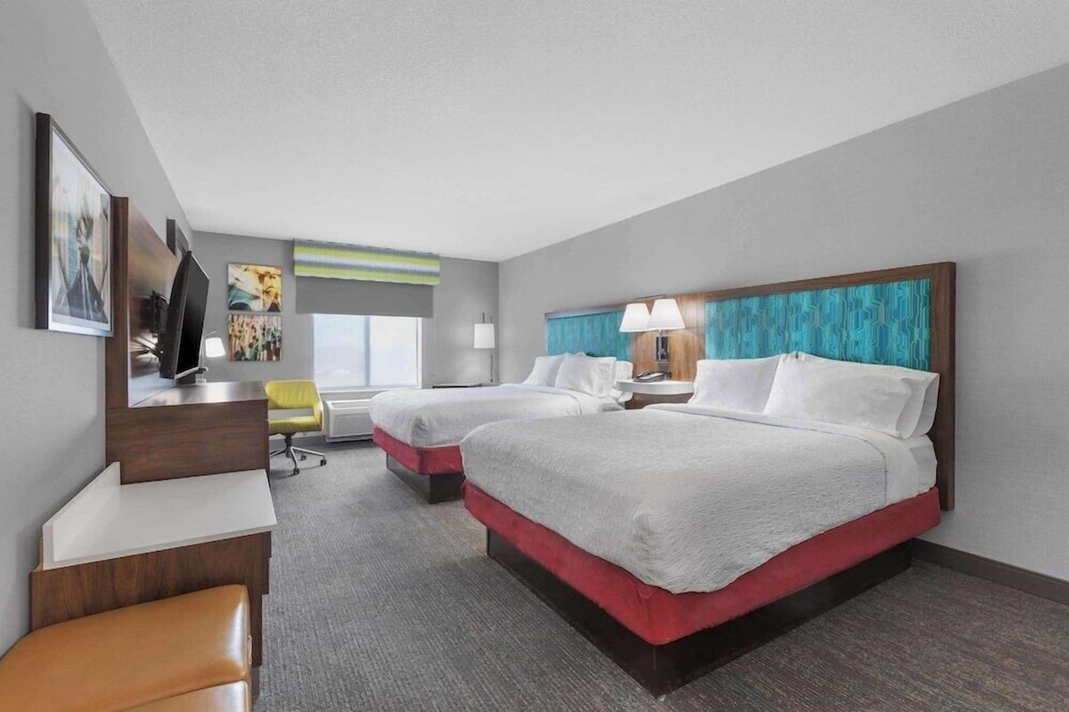 A hotel room with two beds, a desk, a chair, and a TV.