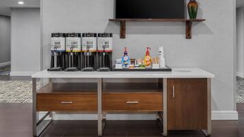 A coffee station with four dispensers labeled 'Dark Roast,' 'Light Roast,' 'Decaf,' and 'Hot Water.' There are also two coffee makers and a selection of coffee creamer bottles.