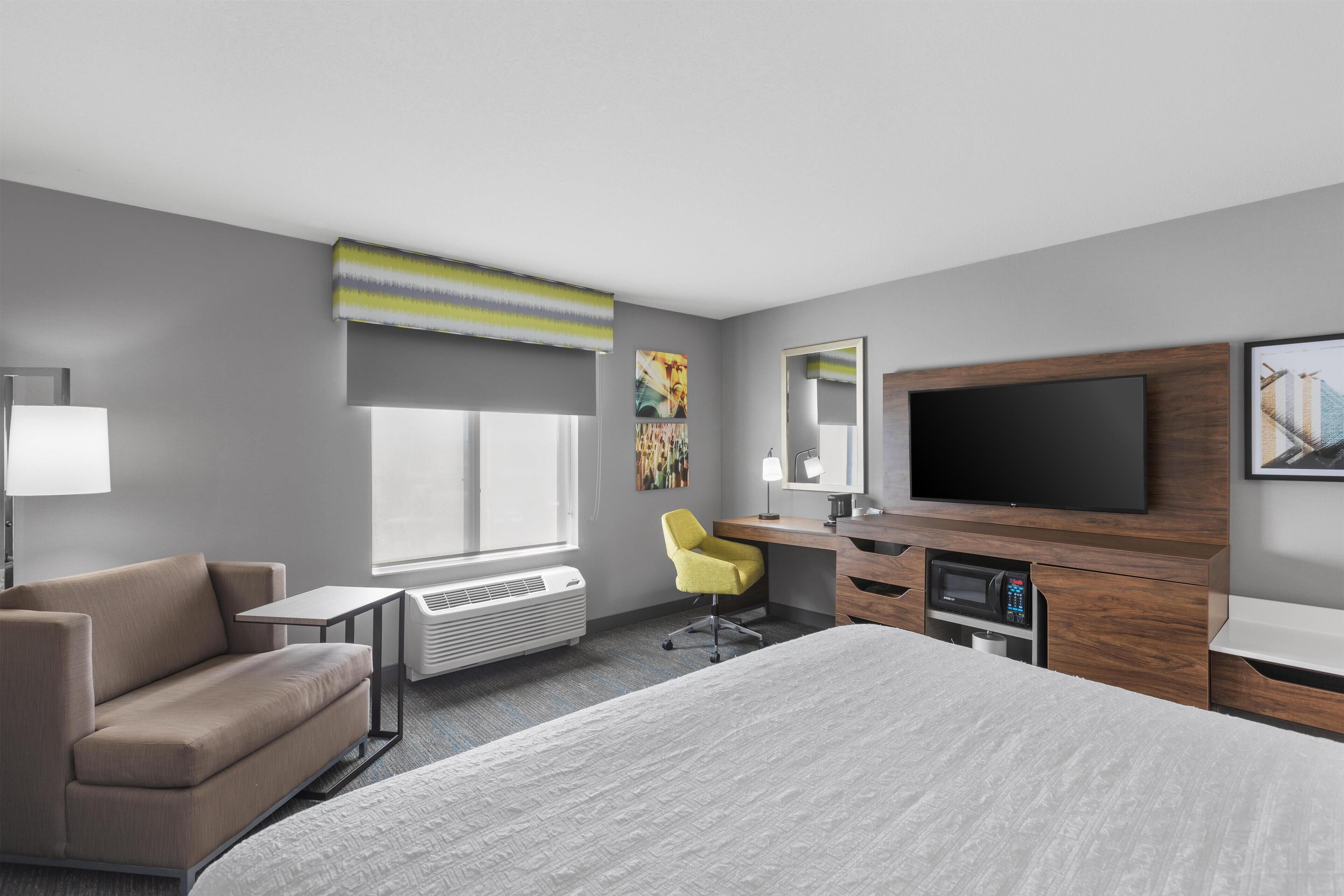 Una habitación de hotel moderna con una cama grande, un sofá, un escritorio con ordenador, un televisor de pantalla plana y una ventana con vistas.