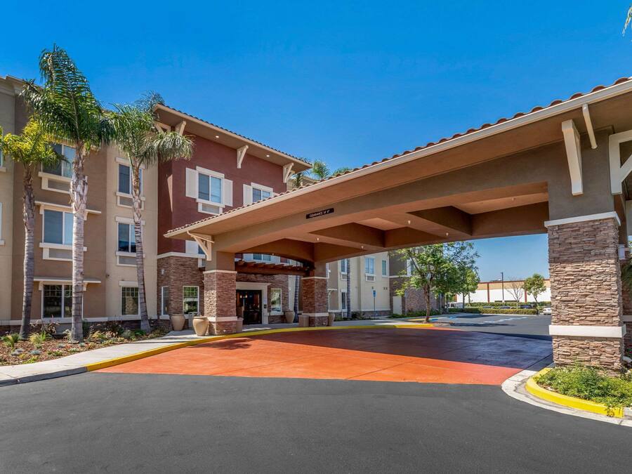 Entrada de hotel con un corredor techado, palmeras y un cielo azul despejado.