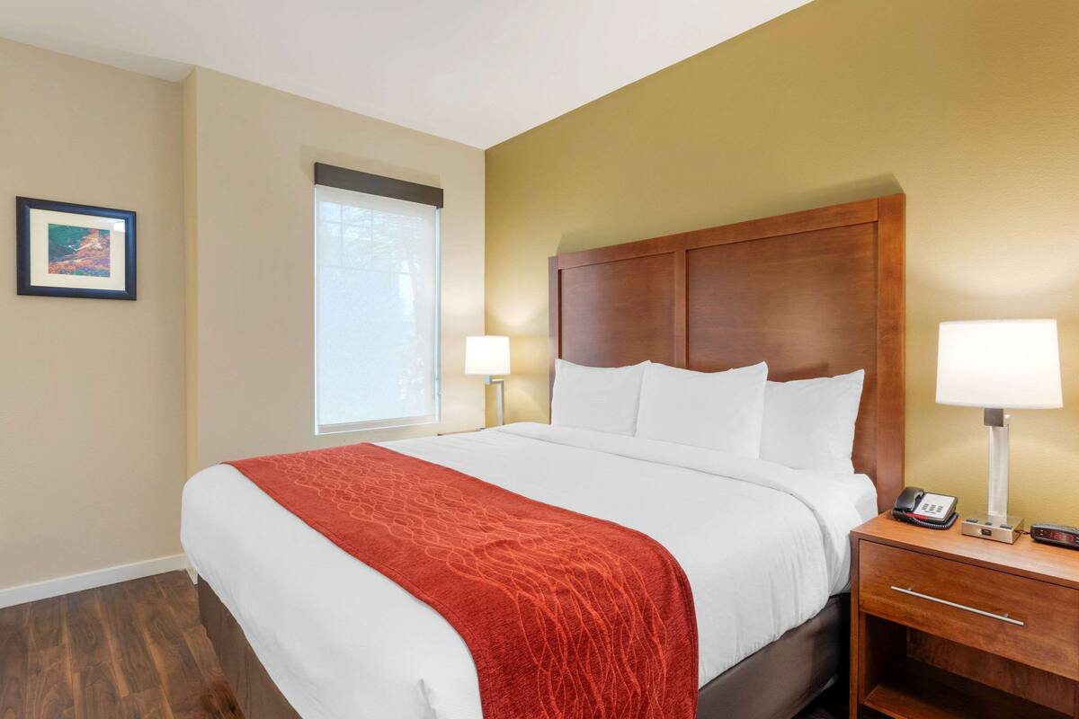 Een hotelkamer met een groot bed, een houten hoofdbord, een nachtkastje met een lamp en een lijst op de muur.