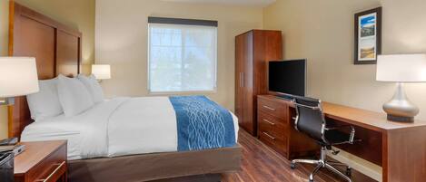 A hotel room with a bed, a desk, a chair, a TV, and a window with blinds.