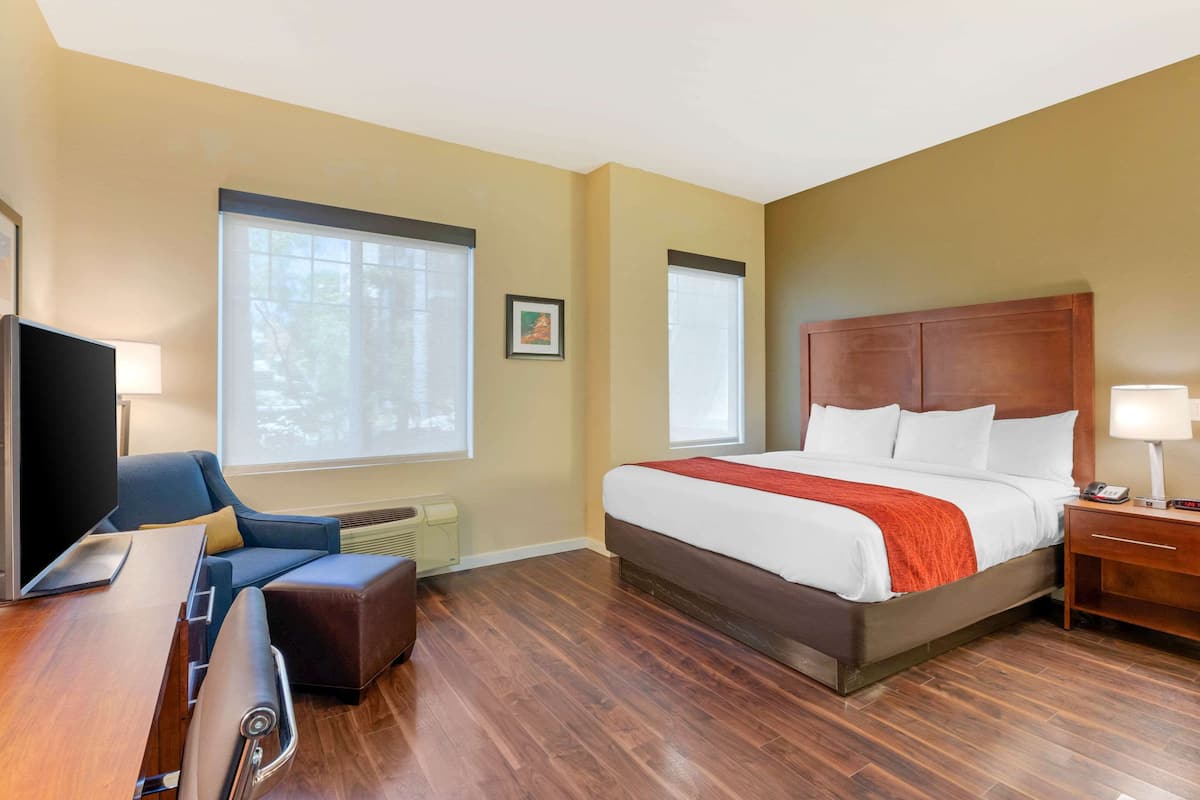 Een hotelkamer met een bed, een bureau met stoel, een televisietoestel en een raam met jaloezieën.