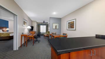 Habitación de hotel con cama, escritorio, sillas, una mesita y un área de kitchenette.