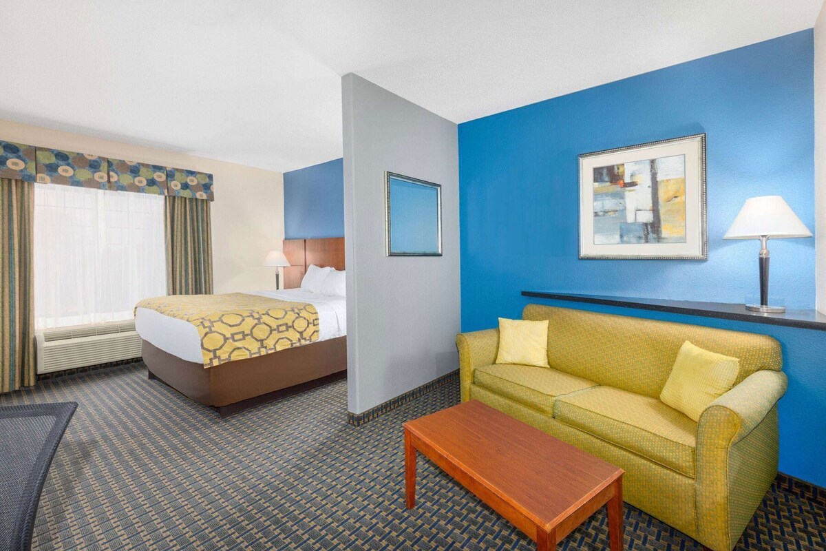 A hotel room with a bed, a sofa, a table, and a window with curtains.