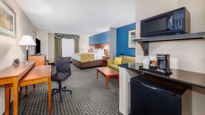 A hotel room with a bed, a desk, a chair, a sofa, a microwave, a coffee maker, and a refrigerator. - Baymont by Wyndham Pratt (Pratt)