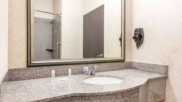 A bathroom with a granite countertop, a sink, a mirror, and a shower visible in the background.