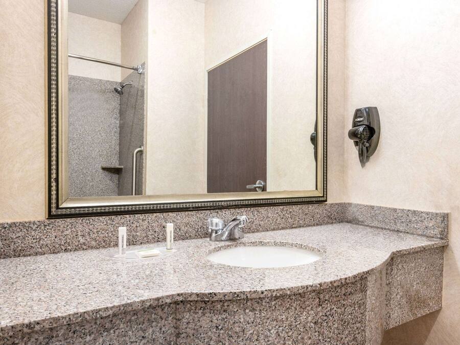 A bathroom with a granite countertop, a sink, a mirror, and a shower visible in the background.