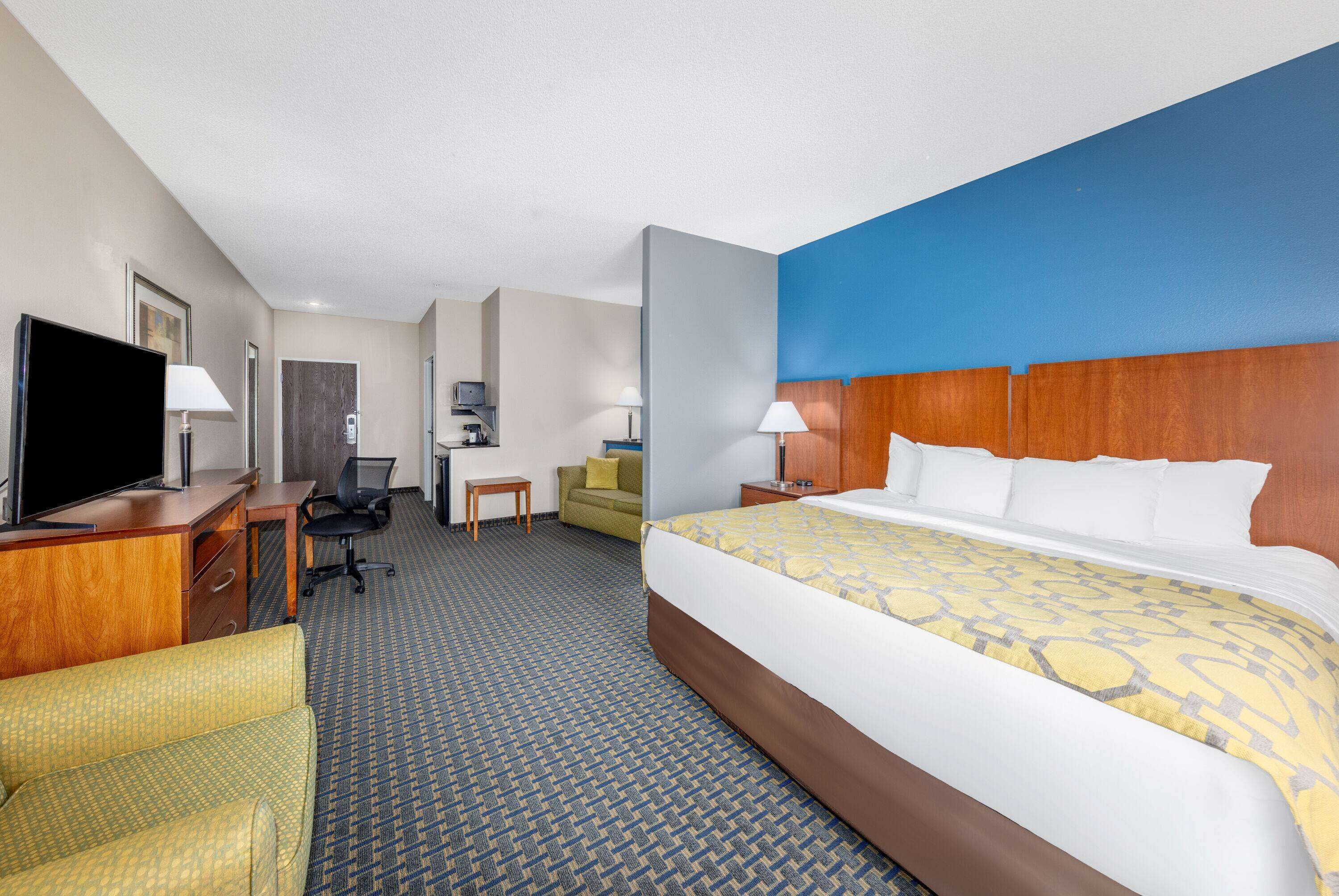 Une chambre d’hôtel avec un grand lit, un bureau avec un ordinateur, une télévision, un canapé et une petite table.