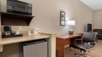 A compact hotel room with a kitchenette, including a microwave, coffee maker, and refrigerator. There is a desk with a chair and a television.
