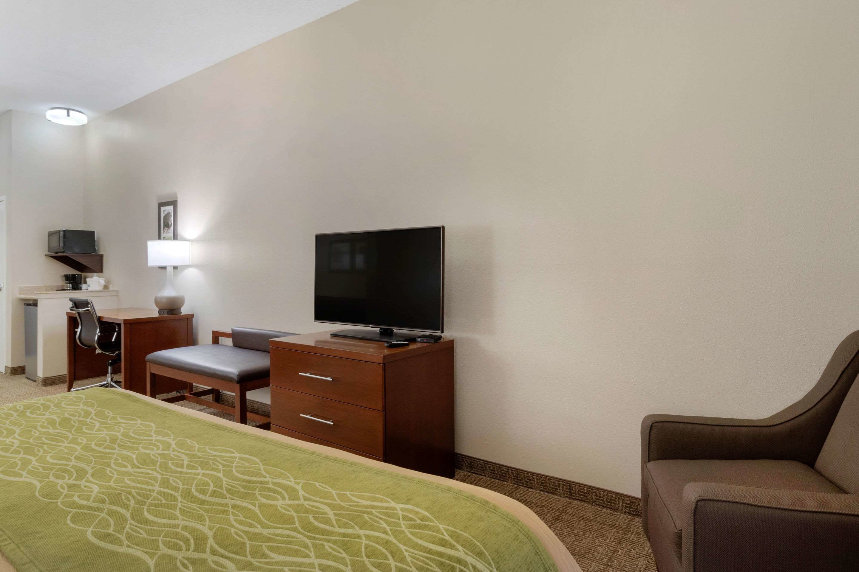 A hotel room with a bed, a desk with a chair, a television, and a lamp.