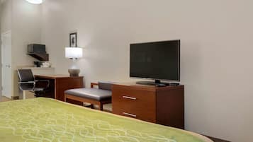 Habitación de hotel con una cama, un escritorio con silla, televisor, lámpara y un estante con microondas.