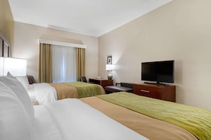 Ein Hotelzimmer mit zwei Betten, einem Schreibtisch, einem Fernseher und einem fensterbepflanzten Fenster.