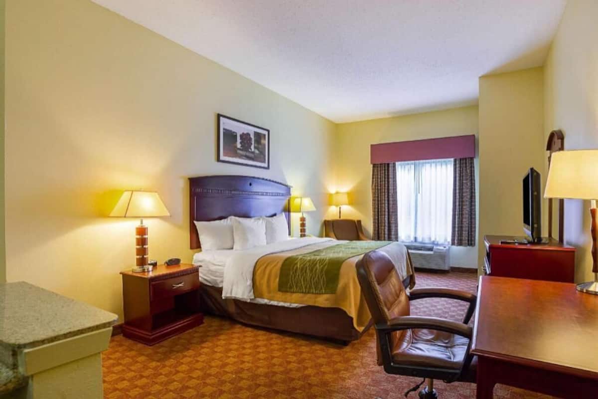 A hotel room with a bed, a desk, a chair, two bedside lamps, a television, and a window with curtains.