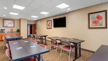 Une salle de conférence équipée de tables et de chaises, d’un téléviseur fixé au mur et de tableaux encadrés.