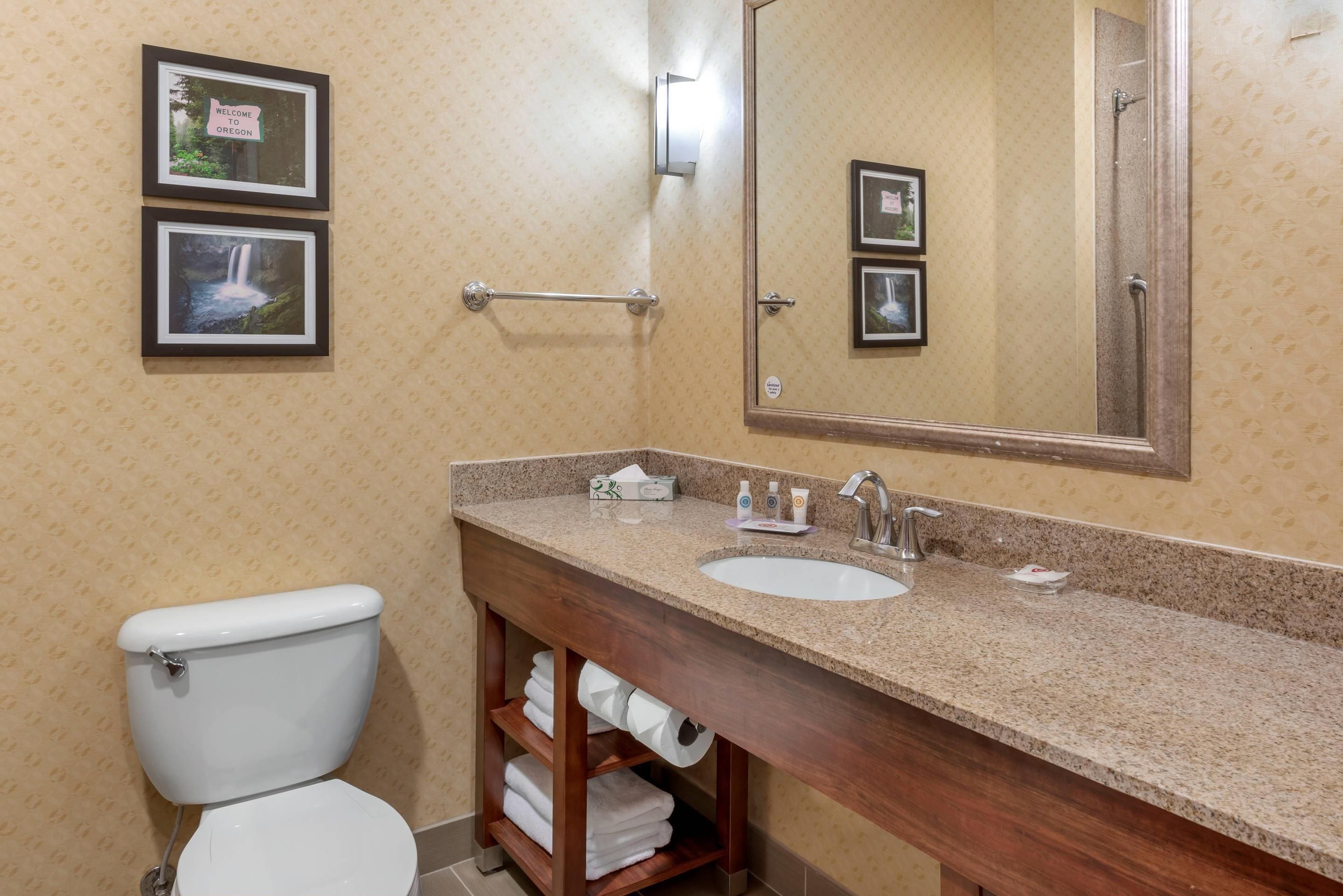 Une salle de bain avec des toilettes, un lavabo et un miroir. Des tableaux encadrés ornent le mur.