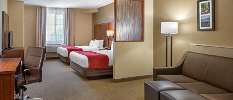 A hotel room with a bed, a desk, a chair, a sofa, a lamp, and a picture on the wall.