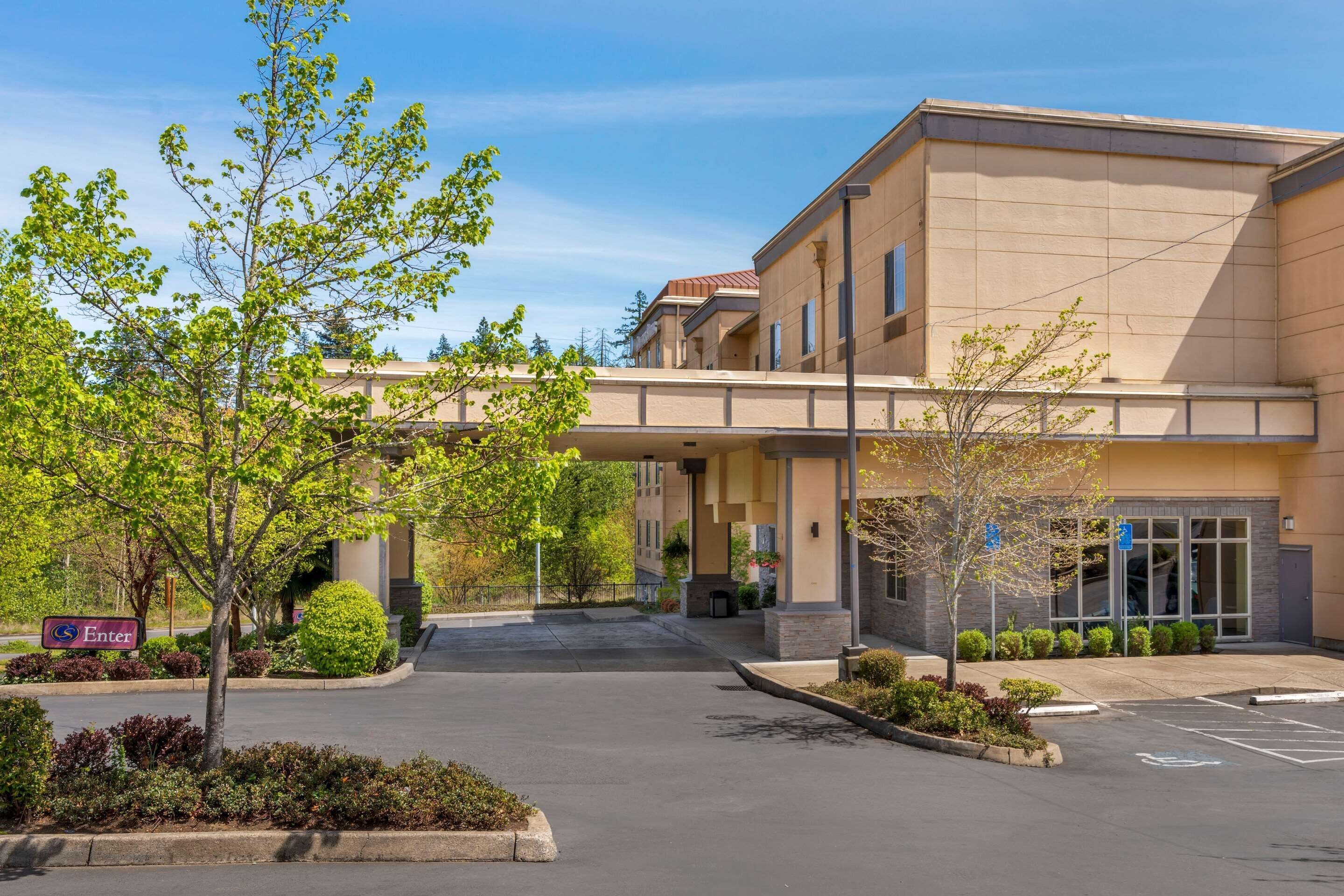 A hotel entrance with a covered walkway, parking lot, and landscaped areas.