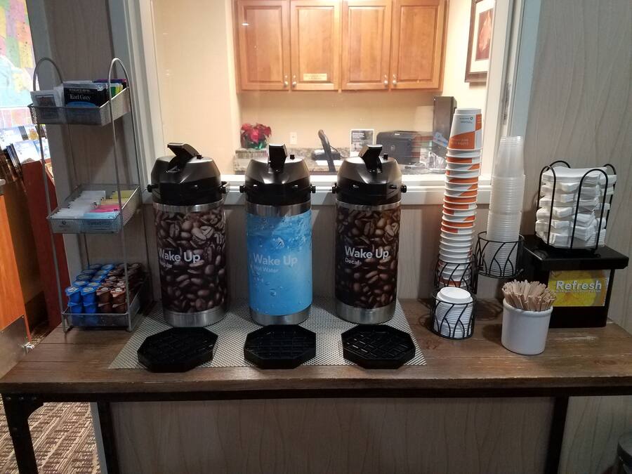 Una estación de café con tres termos etiquetados como 'Despierta': uno con granos de café descafeinado, uno con agua caliente y uno con granos de café regular.