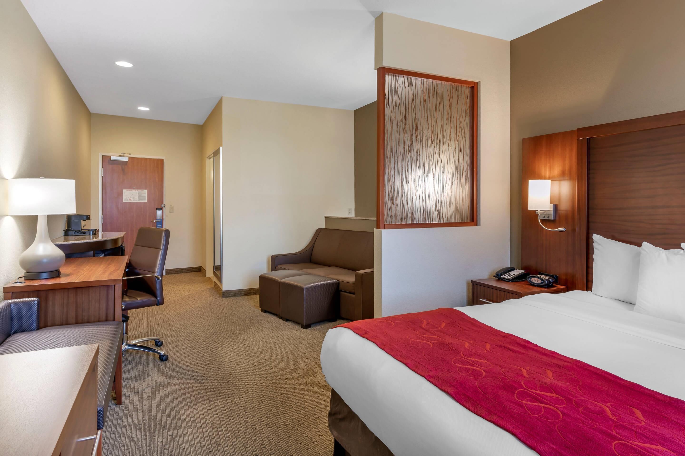 A hotel room with a large bed, a desk with a chair, a small sofa, a nightstand with a phone, and a wall-mounted lamp.
