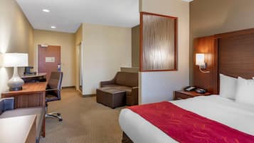 A hotel room with a large bed, a desk with a chair, a small sofa, a nightstand with a phone, and a wall-mounted lamp.