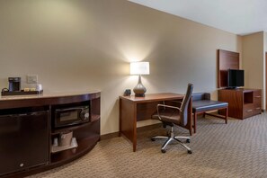 Une chambre d’hôtel équipée d’un bureau en bois, d’une chaise, d’une lampe, d’une télévision, d’un four à micro-ondes et d’une machine à café.