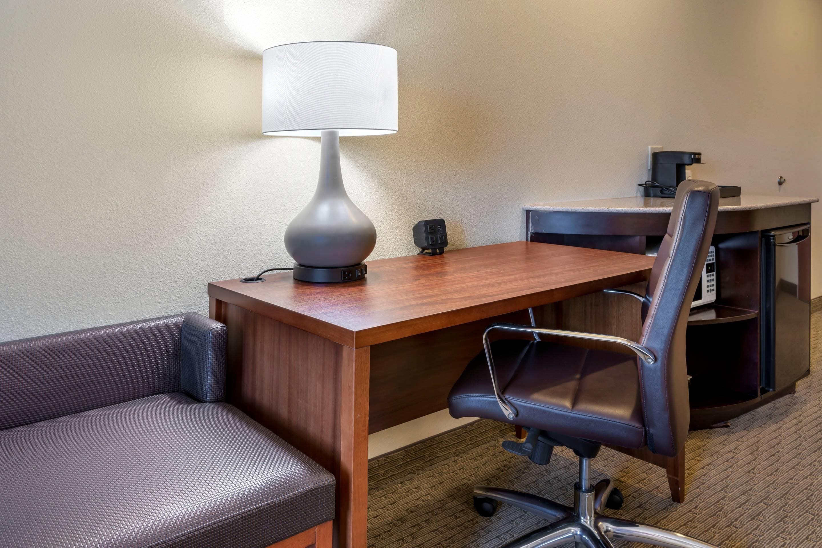 Une chambre d’hôtel avec un bureau en bois, un fauteuil de bureau noir, une lampe, une petite enceinte noire et une machine à café.