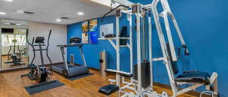 Een sportschool met diverse fitnessapparaten, een loopband en een spiegel.