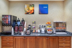 Zona de desayuno de hotel con una máquina de café, dispensadores de café, fruteros y una estación de zumos.