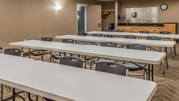 Una sala de conferencias con varias mesas y sillas, una zona de kitchenette y un reloj en la pared.