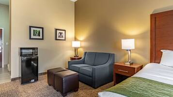 A hotel room with a bed, a sofa, a desk, a lamp, a microwave, and a refrigerator.