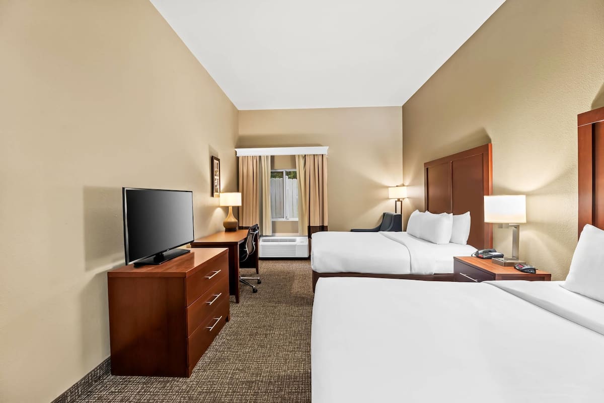 A hotel room with two beds, a desk with a TV, a dresser, and a window with curtains.