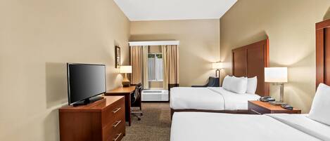 A hotel room with two beds, a desk with a TV, a dresser, and a window with curtains.