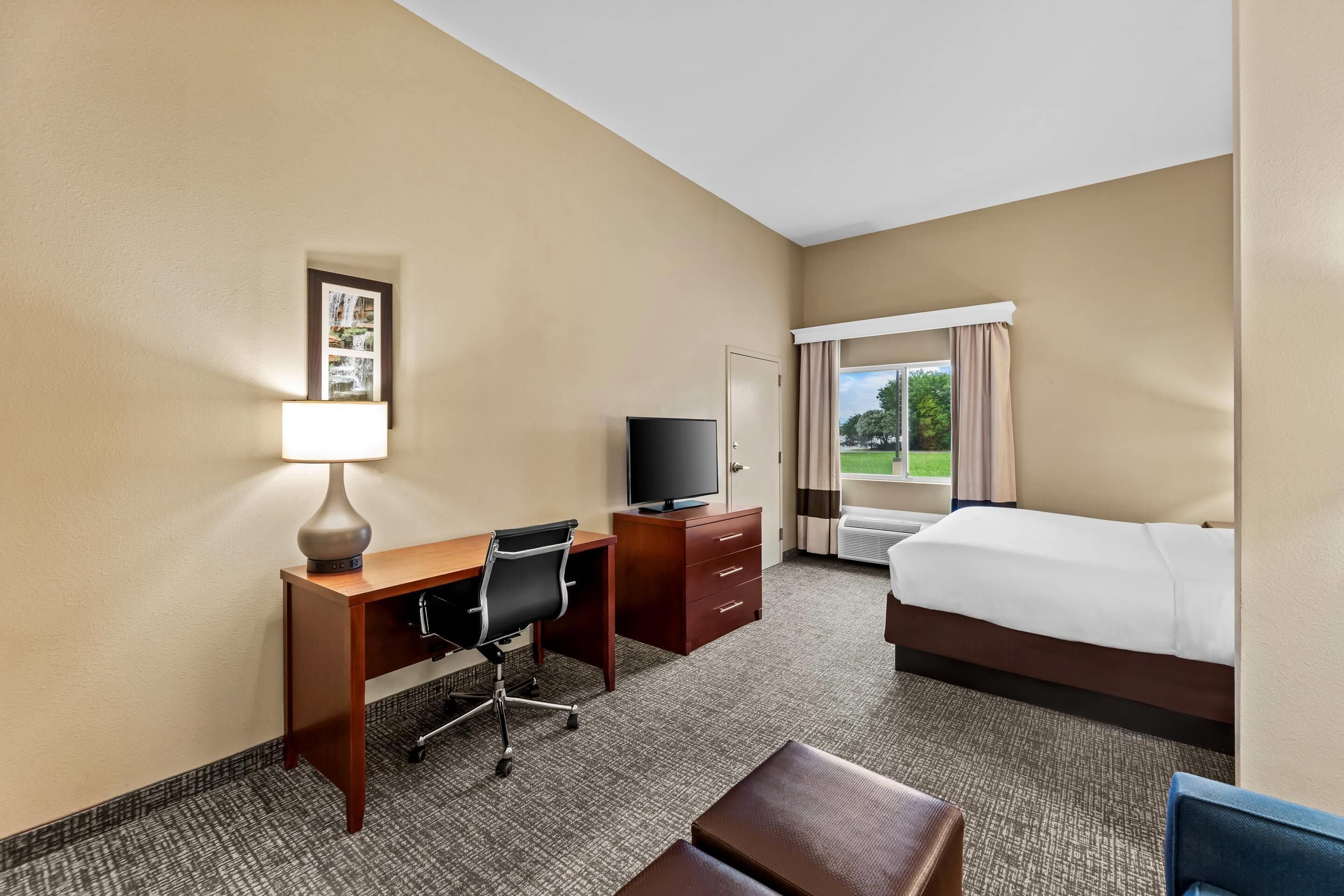 A hotel room with a bed, desk, chair, TV, and a window with curtains.