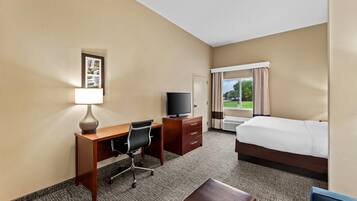 A hotel room with a bed, desk, chair, TV, and a window with curtains.
